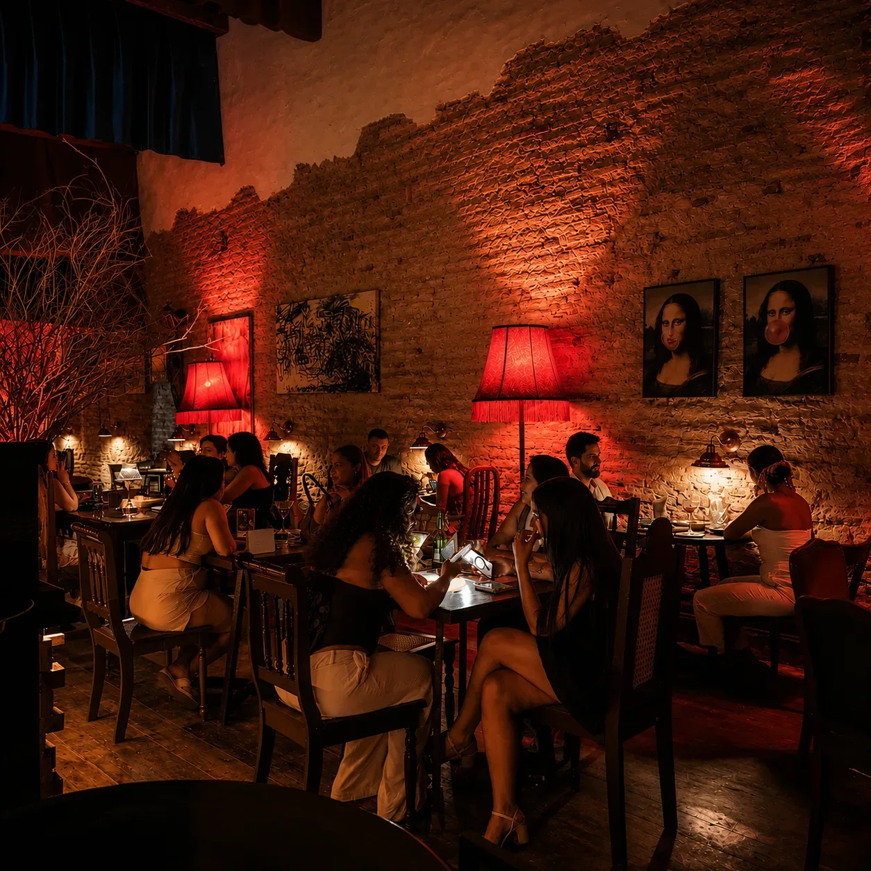 Salão do BICA BAR à noite, sob luz âmbar e vermelha, com paredes de tijolo colonial, quadros da Mona Lisa e clientes às mesas